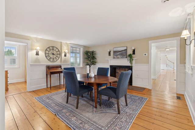 dining room with wainscoting, light wood-style floors, visible vents, and a fireplace