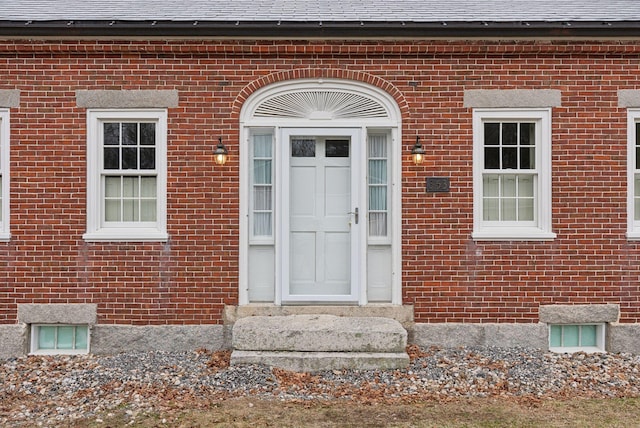 doorway to property featuring brick siding and a shingled roof