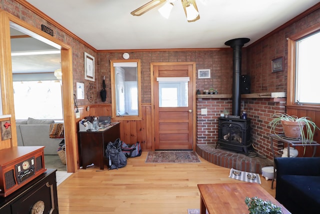 entrance foyer with a ceiling fan, wood finished floors, a wainscoted wall, and a wood stove