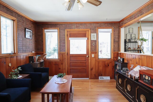 living room featuring light wood-type flooring, wainscoting, a ceiling fan, wooden walls, and ornamental molding