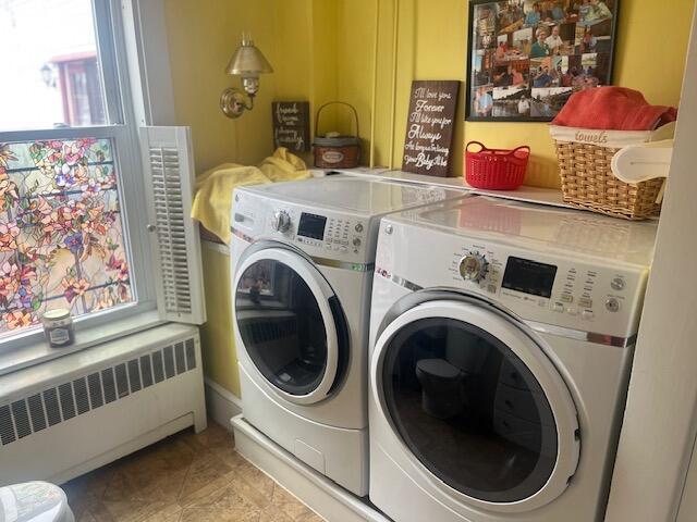 clothes washing area with washing machine and dryer, radiator heating unit, and laundry area