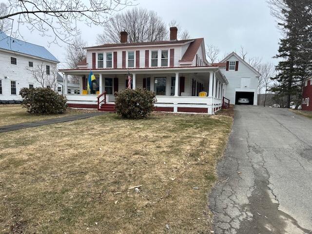 view of front of home with a front yard, covered porch, aphalt driveway, a chimney, and an outdoor structure