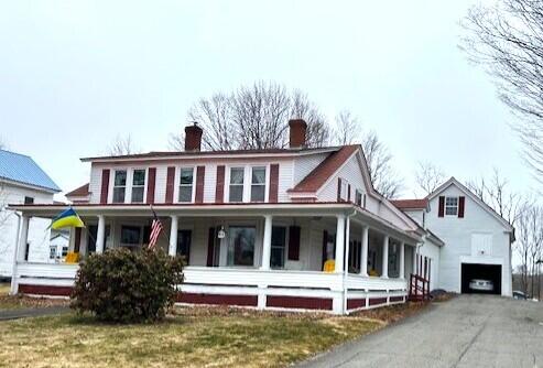 view of front facade featuring aphalt driveway, covered porch, a garage, and a chimney