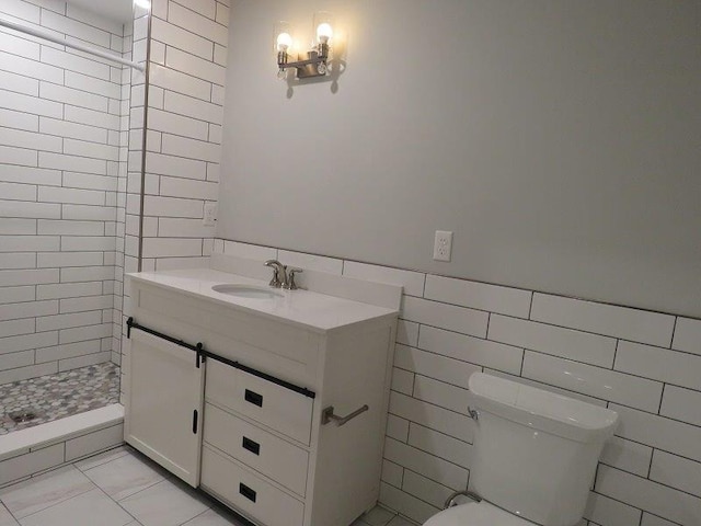 full bath with tile walls, toilet, vanity, wainscoting, and tiled shower