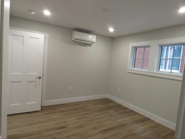 basement featuring recessed lighting, a wall mounted AC, baseboards, and wood finished floors