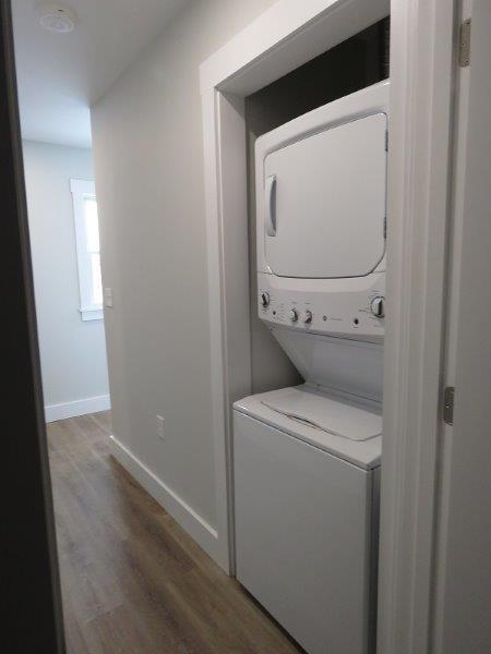 washroom with laundry area, stacked washer and dryer, wood finished floors, and baseboards