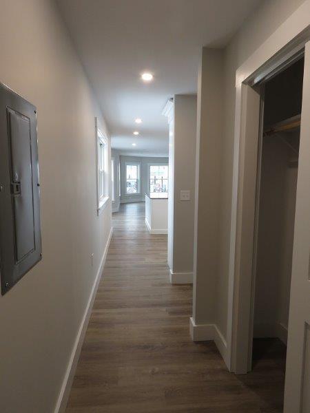 corridor featuring electric panel, recessed lighting, baseboards, and wood finished floors