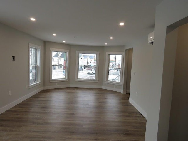 empty room with dark wood-type flooring, a wall mounted air conditioner, baseboards, and recessed lighting