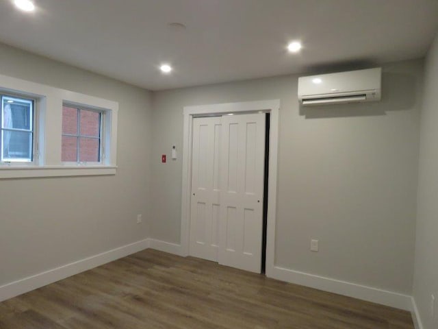 unfurnished bedroom featuring recessed lighting, baseboards, a wall unit AC, and wood finished floors