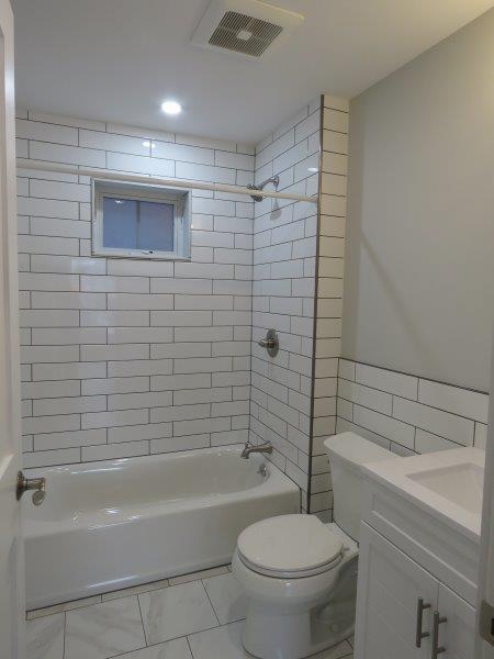 bathroom featuring tile patterned flooring, toilet, visible vents, bathtub / shower combination, and tile walls