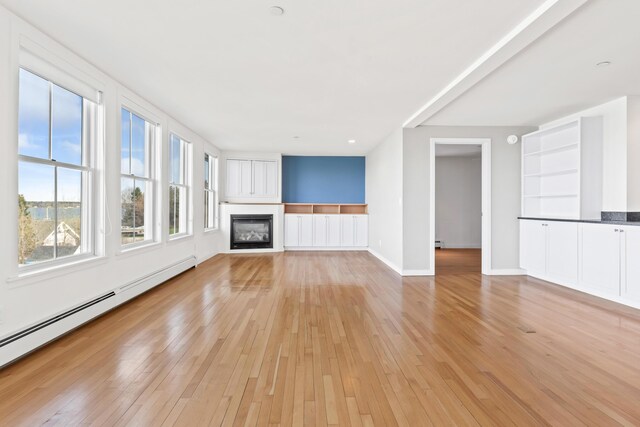 6 Merritt House Rd Unit 20, Harpswell, ME 04066 - unfurnished living room with a baseboard heating unit, light wood-style floors, a glass covered fireplace, and baseboard heating
