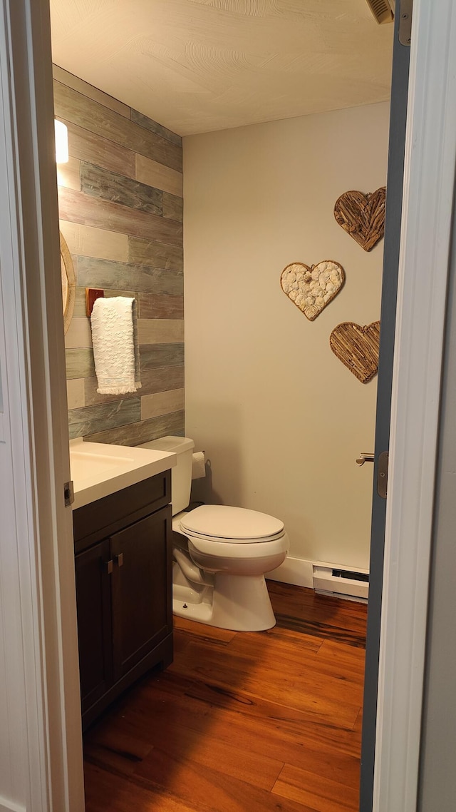 54 Black Smith Rd Unit 13, Wells, ME 04090 - bathroom with wood finished floors, vanity, a baseboard heating unit, toilet, and wooden walls