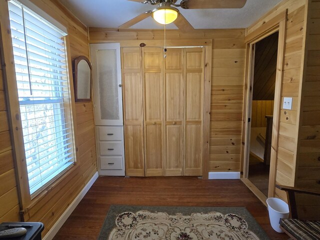 1898 Roxbury Rd, Roxbury, ME 04275 - unfurnished bedroom featuring wooden walls, dark wood-style floors, baseboards, and a ceiling fan