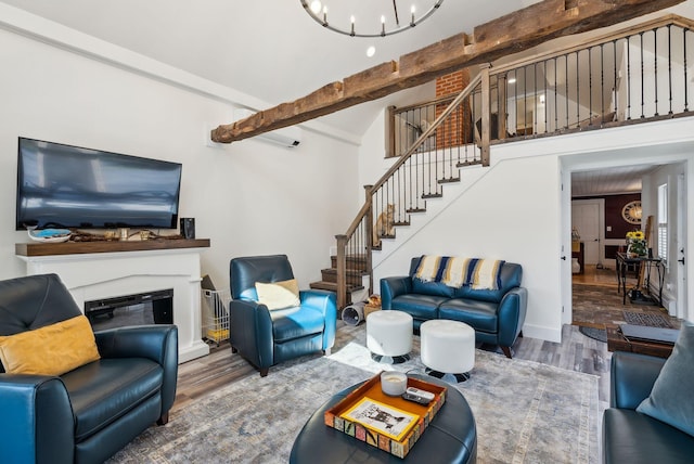 living room featuring a notable chandelier, beam ceiling, a glass covered fireplace, stairs, and wood finished floors