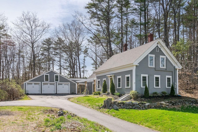 view of front of house featuring a detached garage, a chimney, and a front lawn