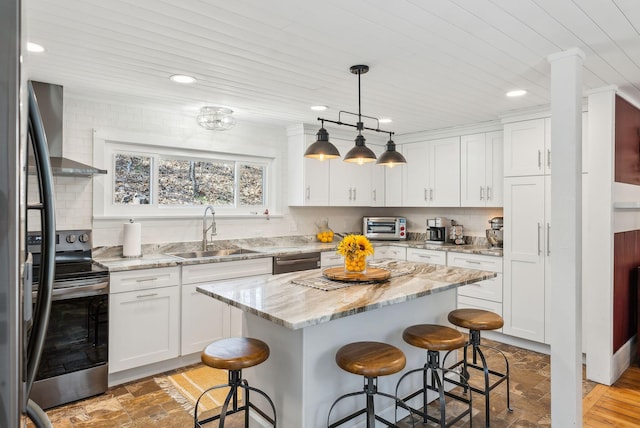 kitchen with wall chimney range hood, a kitchen breakfast bar, appliances with stainless steel finishes, and a sink