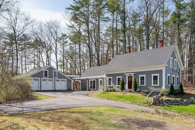 view of front of home featuring a detached garage, a chimney, and a shingled roof