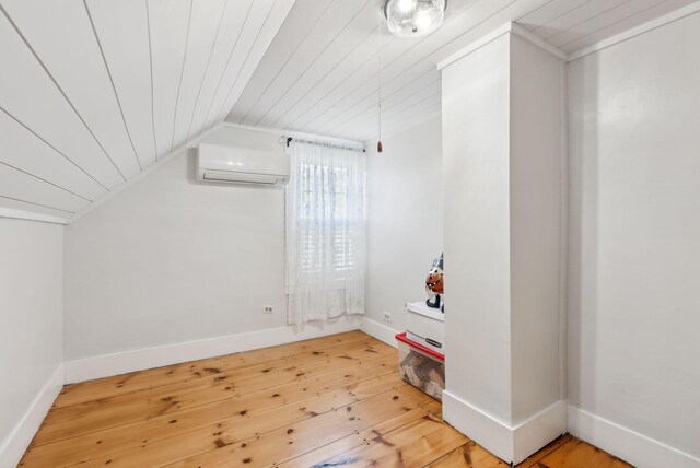 additional living space featuring wooden ceiling, a wall unit AC, vaulted ceiling, and hardwood / wood-style floors