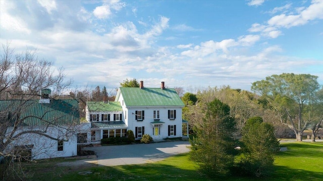 view of front of home with a chimney, metal roof, and a front lawn