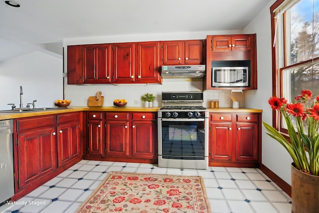 kitchen with appliances with stainless steel finishes, under cabinet range hood, reddish brown cabinets, and light floors