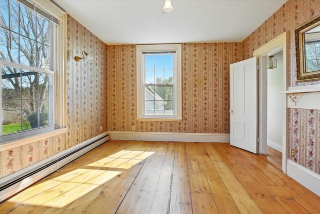 unfurnished room featuring baseboards, a healthy amount of sunlight, hardwood / wood-style flooring, and a baseboard radiator