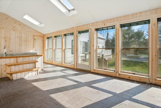 unfurnished sunroom featuring wood walls, lofted ceiling with skylight, and stone tile flooring
