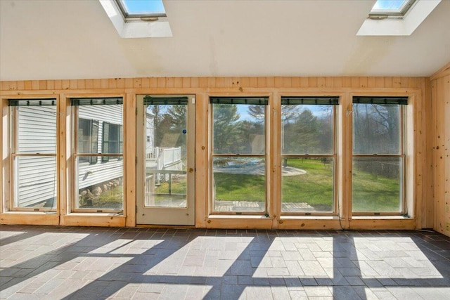 entryway featuring wood walls, lofted ceiling with skylight, and stone tile flooring