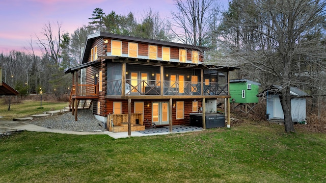 back of property at dusk featuring a lawn, a sunroom, and a hot tub