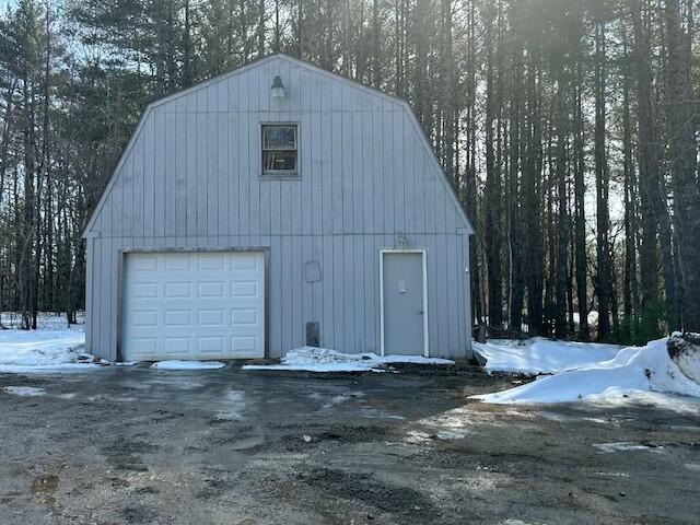 snow covered garage with a wooded view and a garage
