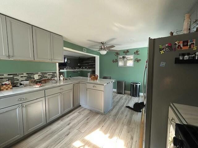 kitchen featuring a peninsula, freestanding refrigerator, backsplash, light wood-style floors, and a ceiling fan