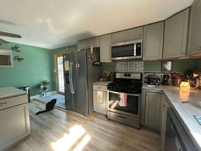 kitchen featuring light countertops, light wood-type flooring, gray cabinets, and stainless steel appliances