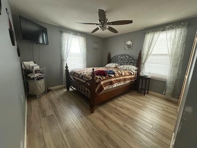 bedroom with light wood-style floors, a ceiling fan, and baseboards