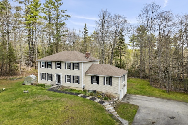 view of front facade with asphalt driveway, a chimney, a shingled roof, an attached garage, and a front yard