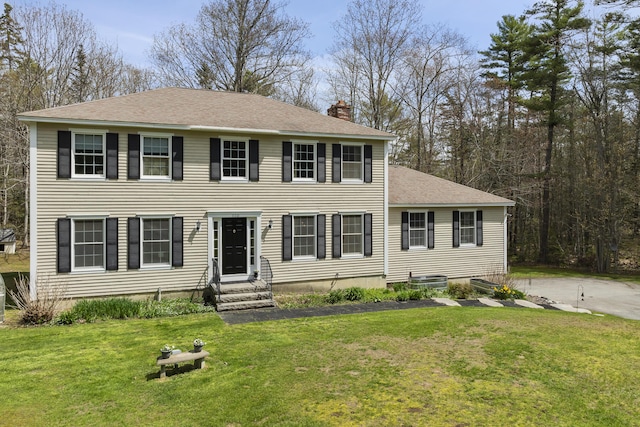 colonial house with entry steps, a chimney, a front yard, and a shingled roof