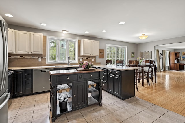 kitchen featuring stainless steel appliances, a sink, light countertops, tasteful backsplash, and dark cabinets