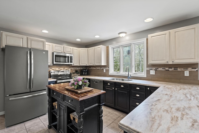 kitchen with appliances with stainless steel finishes, a sink, dark cabinets, light tile patterned flooring, and backsplash