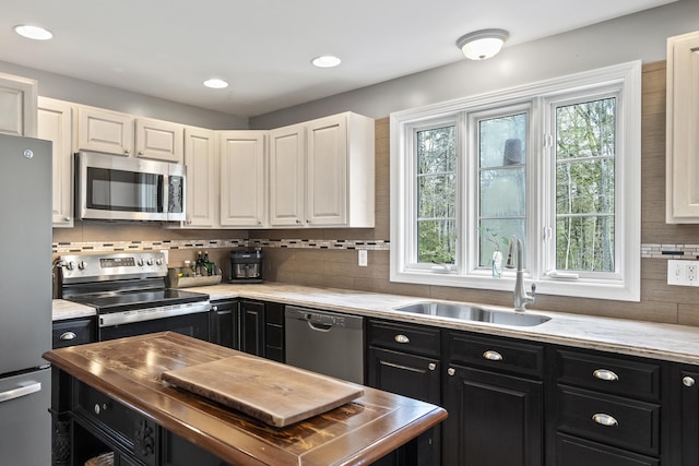 kitchen with stainless steel appliances, dark cabinetry, a sink, backsplash, and recessed lighting