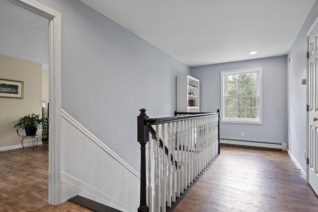 corridor featuring baseboard heating, an upstairs landing, wood finished floors, and baseboards