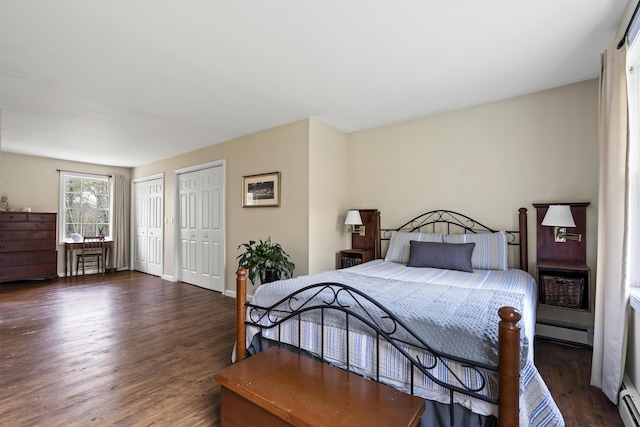 bedroom with baseboard heating, multiple closets, wood finished floors, and baseboards