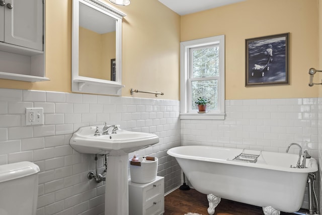 full bathroom with tile walls, a freestanding bath, a wainscoted wall, toilet, and wood finished floors