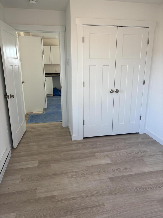unfurnished bedroom with light wood-type flooring, baseboards, a closet, and a baseboard heating unit