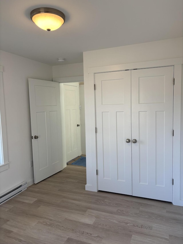 unfurnished bedroom with a baseboard radiator, light wood-type flooring, and a closet