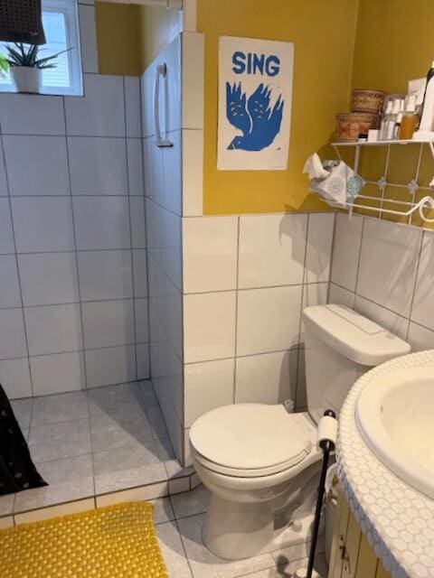 bathroom with tile walls, tiled shower, toilet, tile patterned floors, and vanity