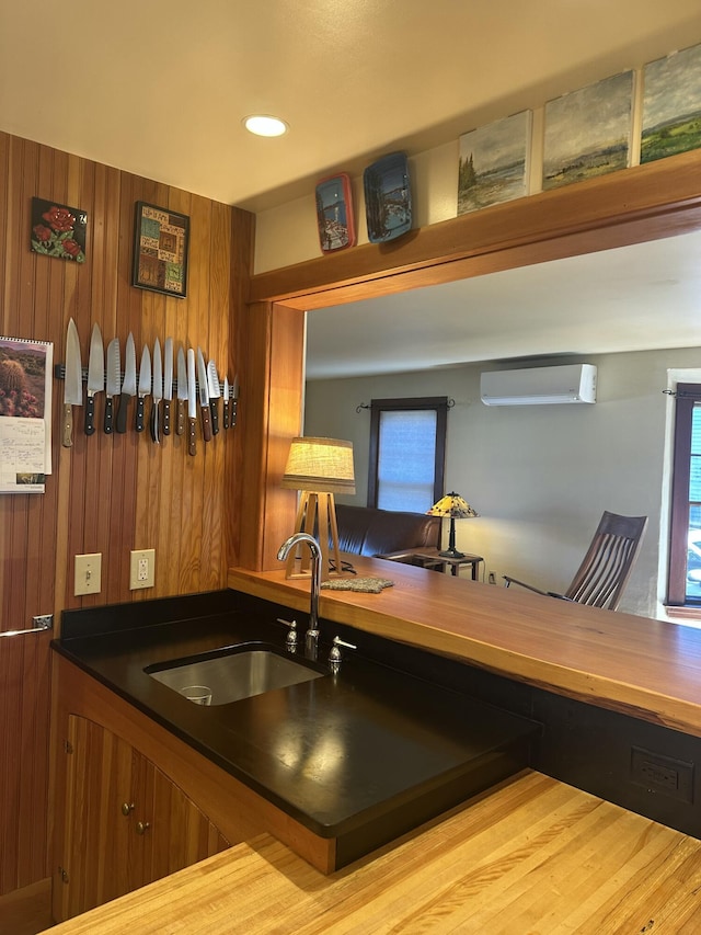 kitchen featuring a wall mounted air conditioner, a sink, brown cabinetry, wooden walls, and recessed lighting