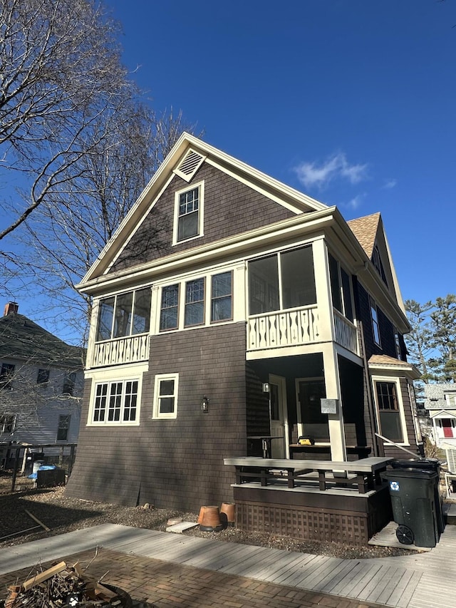 back of house with a sunroom, an outdoor fire pit, and a shingled roof