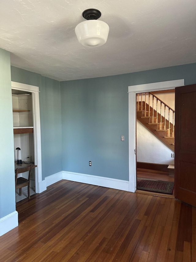 unfurnished room featuring hardwood / wood-style floors, baseboards, built in features, and stairs