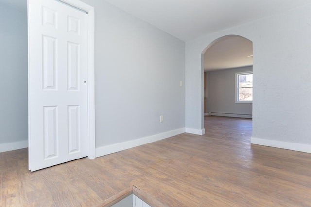 unfurnished room with arched walkways, wood finished floors, baseboards, and baseboard heating