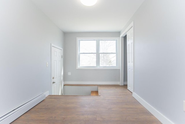 corridor featuring a baseboard radiator, baseboards, and wood finished floors