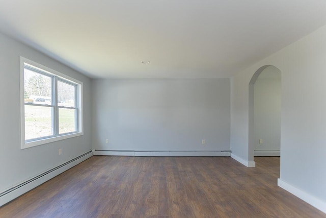 spare room with a baseboard heating unit, dark wood finished floors, and arched walkways