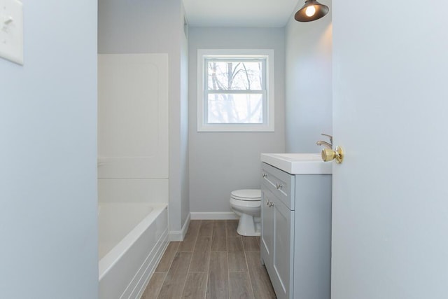 bathroom featuring a washtub, wood tiled floor, vanity, baseboards, and toilet